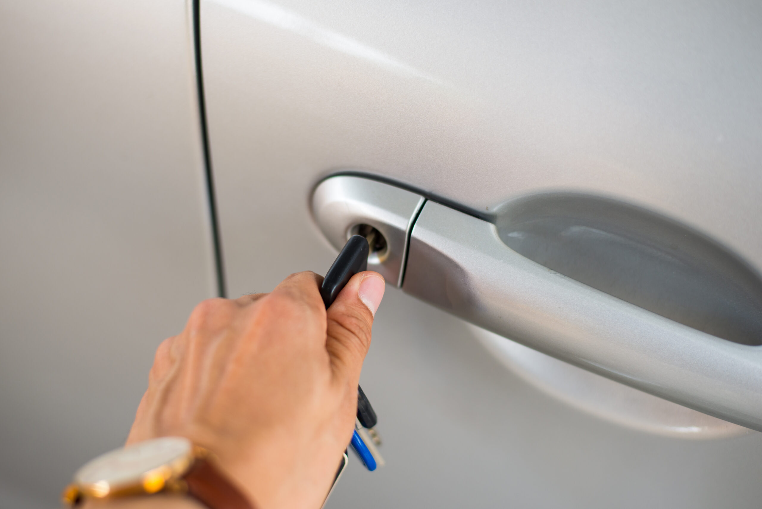 Close up image. He is using the key to unlock the car's door.